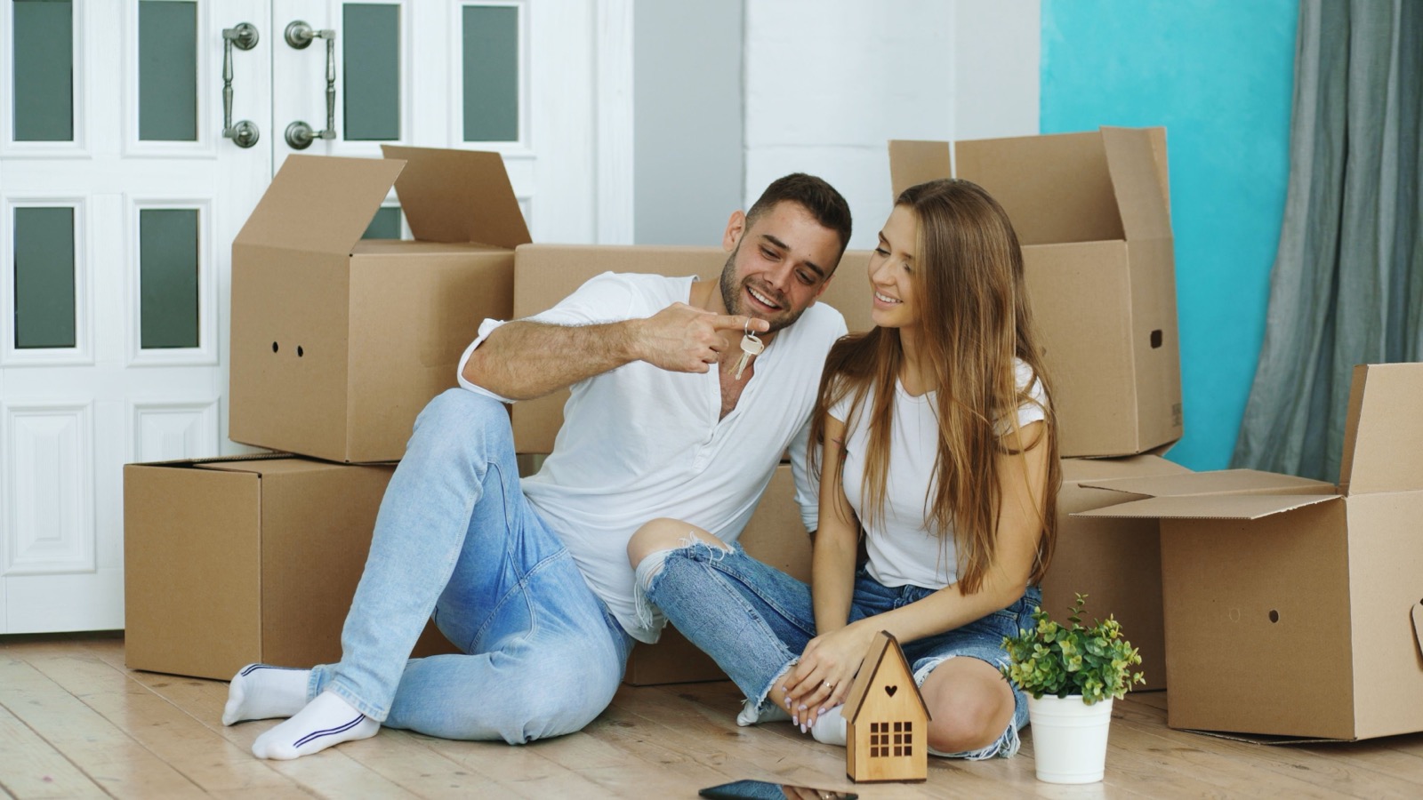 Pareja sentada entre cajas de mudanza en su casa nueva, sosteniendo las llaves