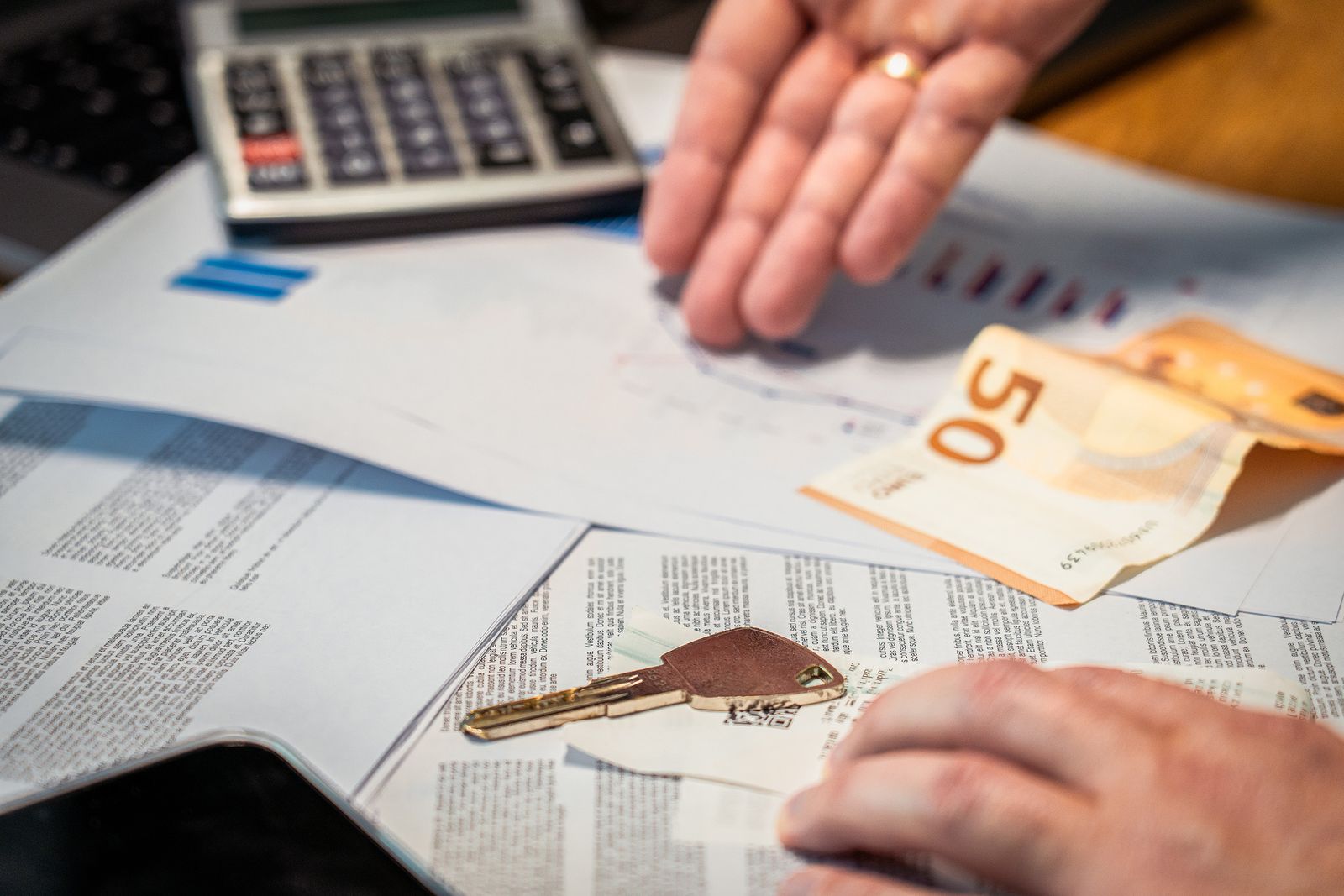 Mesa con calculadora, documentos de compraventa, un billete de 50 euros y la llave de una vivienda