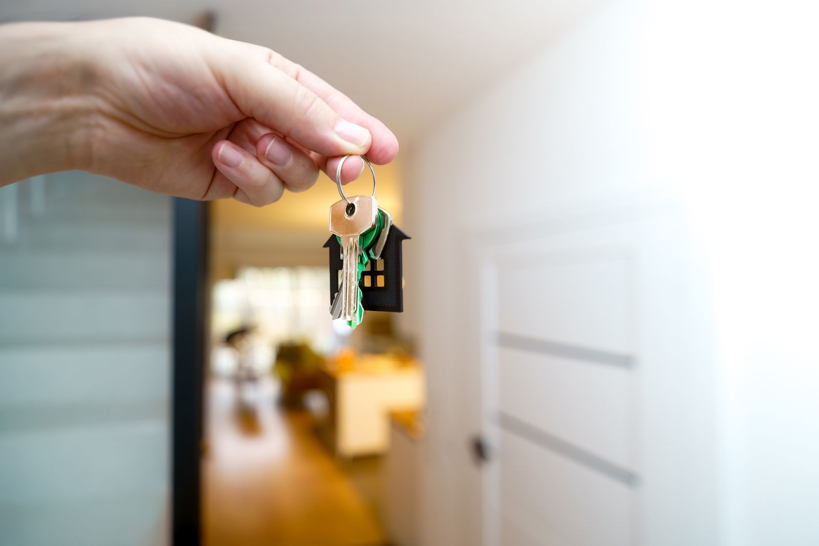 Mano sosteniendo un llavero con varias llaves y un colgante en forma de casa en el recibidor de una vivienda luminosa