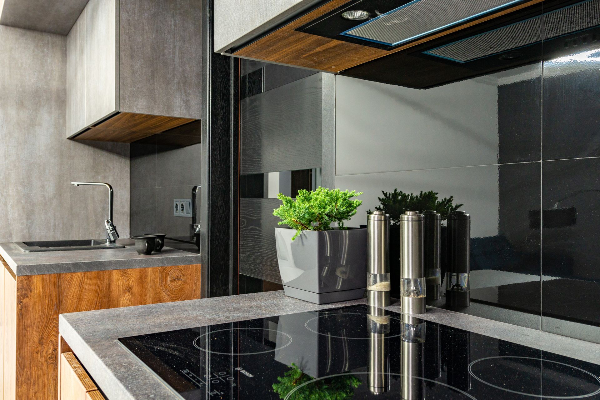Cocina moderna con placa de inducción negra encastrada en encimera gris, campana integrada y frentes de madera