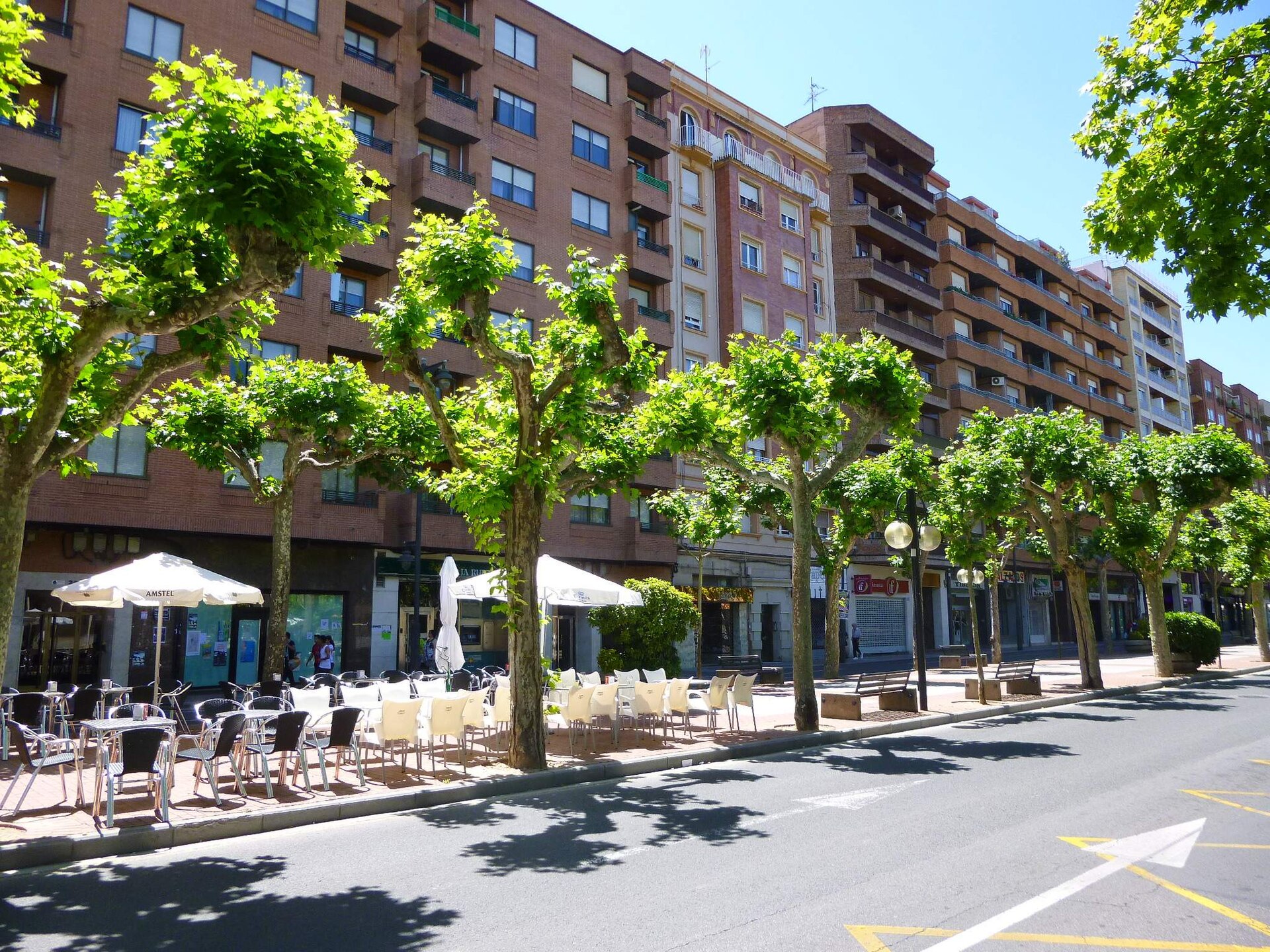 Bloques de viviendas de ladrillo con balcones y terrazas en la Avenida de la Paz de Logroño, con árboles y veladores en la acera