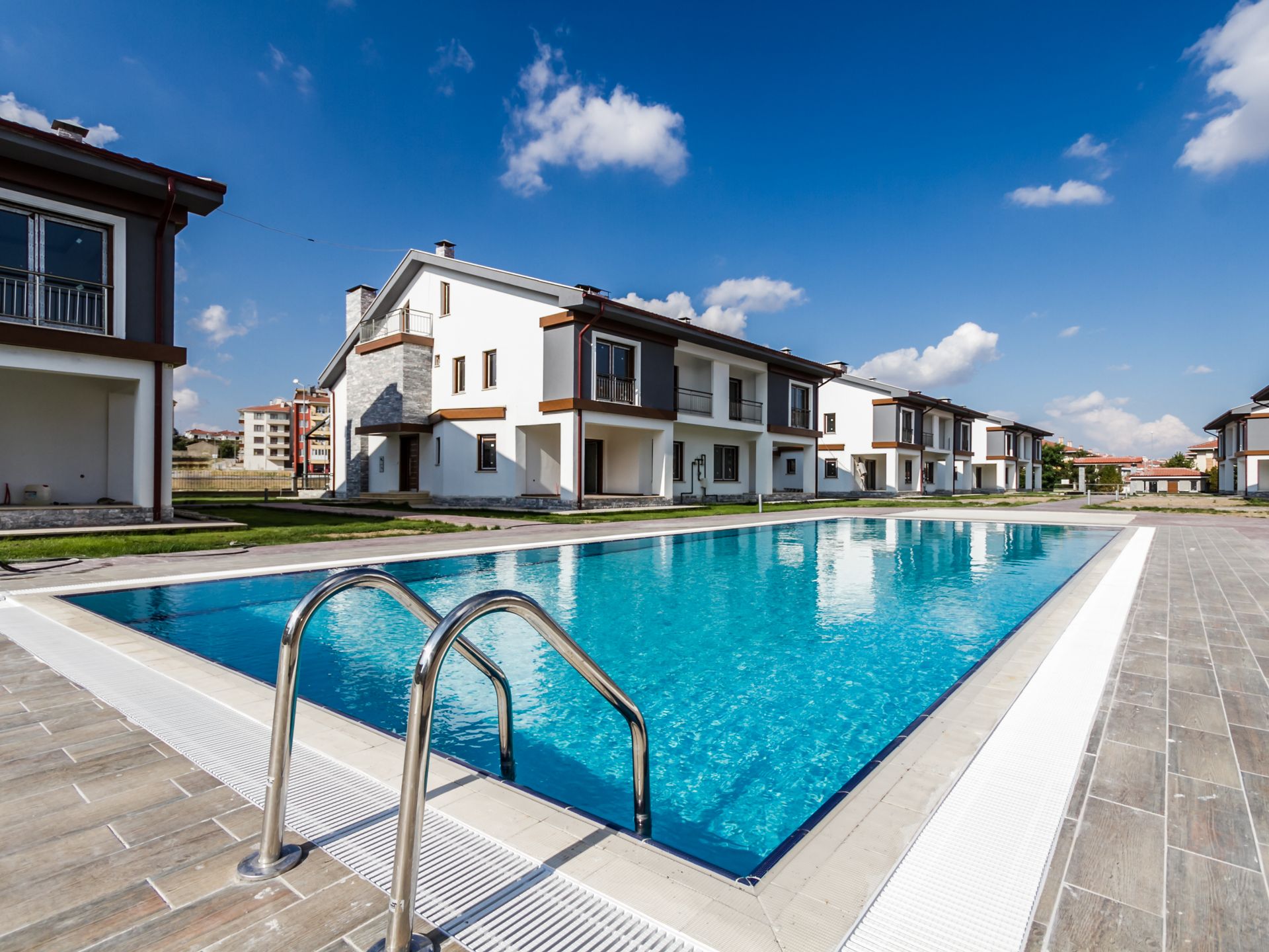 Casas pareadas de obra nueva alrededor de una piscina comunitaria con solería de tarima y cielo azul