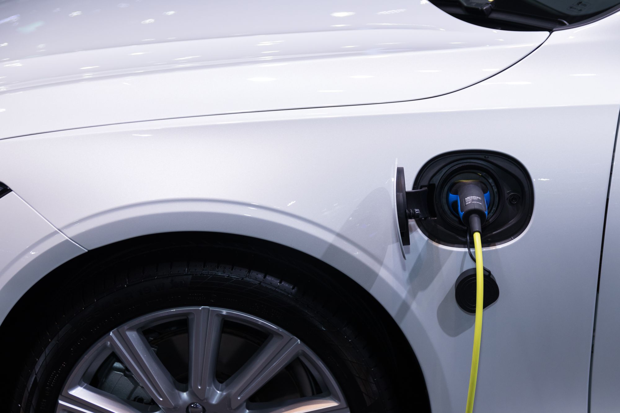 Cable de recarga conectado a la toma de un coche eléctrico blanco aparcado junto a una vivienda