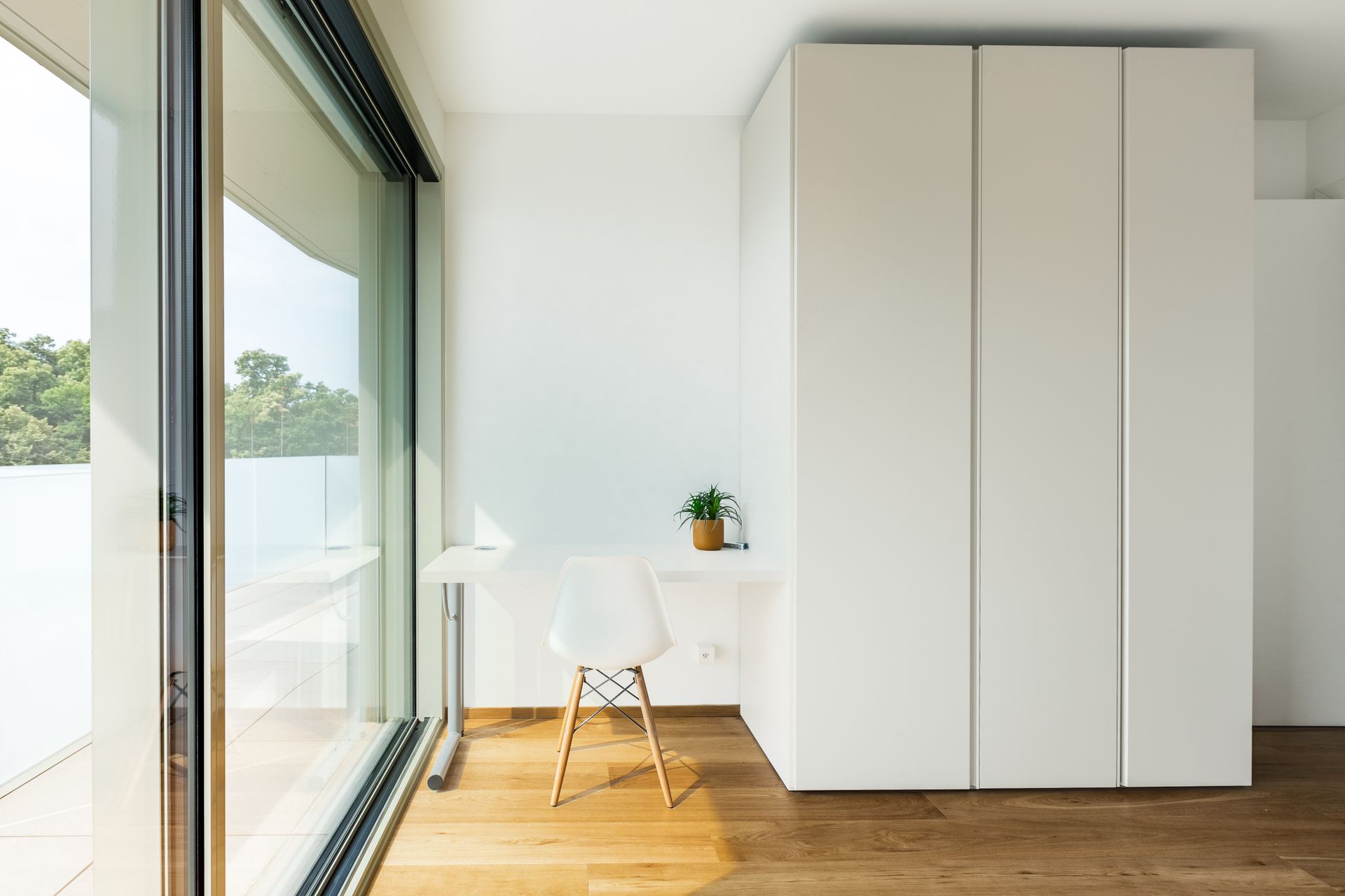Rincón de trabajo con escritorio blanco y silla junto a una gran cristalera en una vivienda de obra nueva